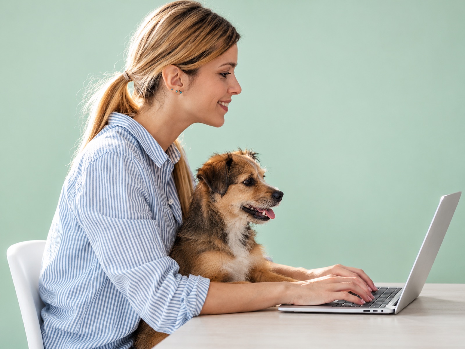 Mujer con su perro en brazos escribiendo en un computador portátil
